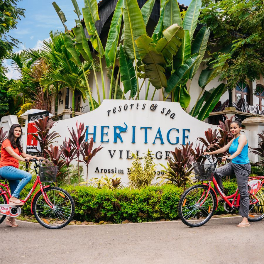 Two women biking at Heritage Village Resorts &amp; Spa, Goa, promoting the Advanced Purchase Rate offer.