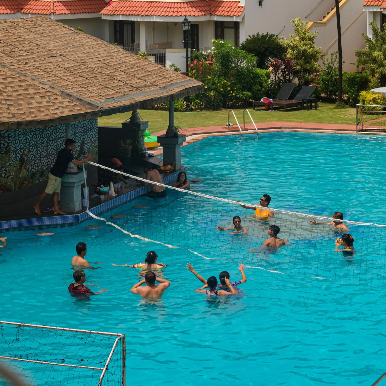 Guests playing throwball in the swimming pool at Heritage Village Goa resort and spa, enjoying the pool and poolside bar.