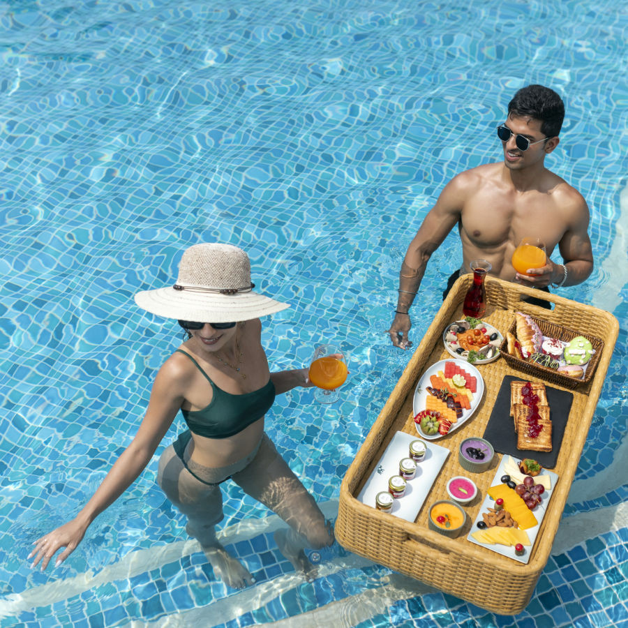 Couple enjoys breakfast in the pool at Heritage Village Resorts &amp; Spa, Goa, highlighting the Stay Longer for Less offer.