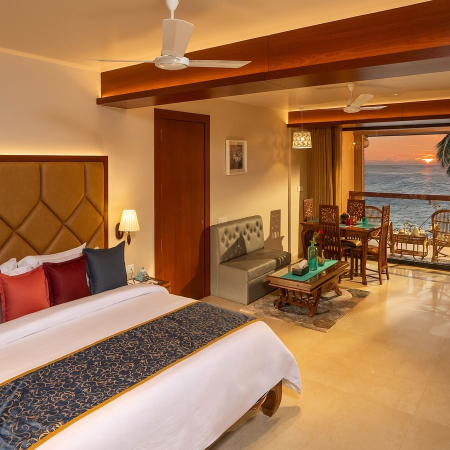 Lounge Seaview Suite at Uday Samudra Leisure Beach Hotel featuring a plush king size bed with colourful pillows, a seating area, and a balcony overlooking the sea at sunset
